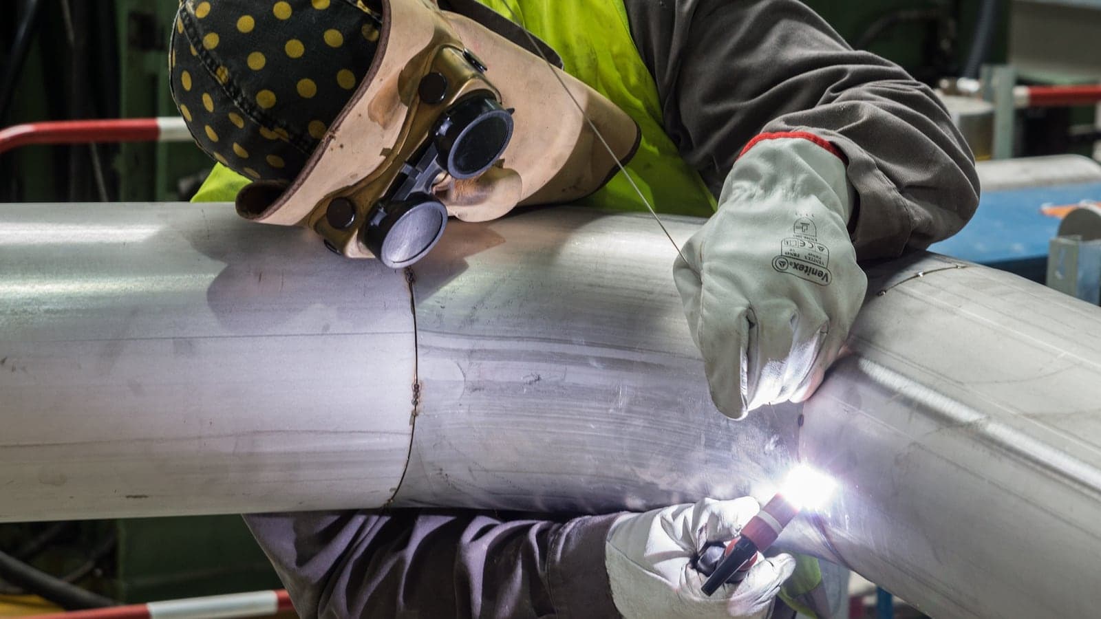 Welder fabricating pipe on a factory shop floor